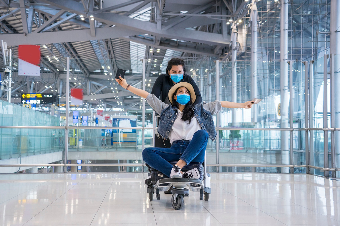 Zwei Freunde die auf einen Kofferwagen an einem Flugplatz in den Urlaub fliegen