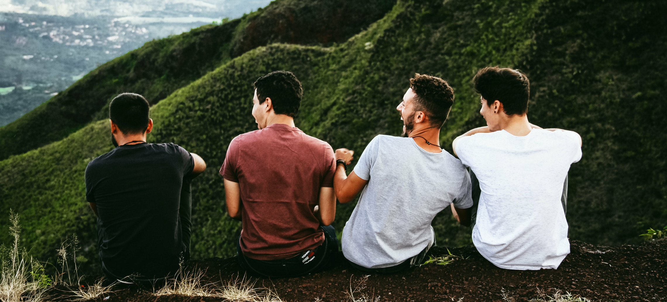 Eine Gruppe von Stedenten sitzen auf einem Felsvorsprung und Lachen, im Hintergrund befindet sich ein bewaldeter Berg