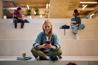 Eine Studentin, die in ihr Handy schaut und an der Uni sitzt. Das Bild zeigt eine Studentin, die an der Uni sitzt und in ihr Handy schaut.