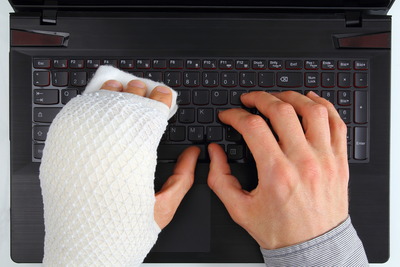 Mann mit einem Gipsarm und einer gesunden Hand tippt auf einer Tastatur