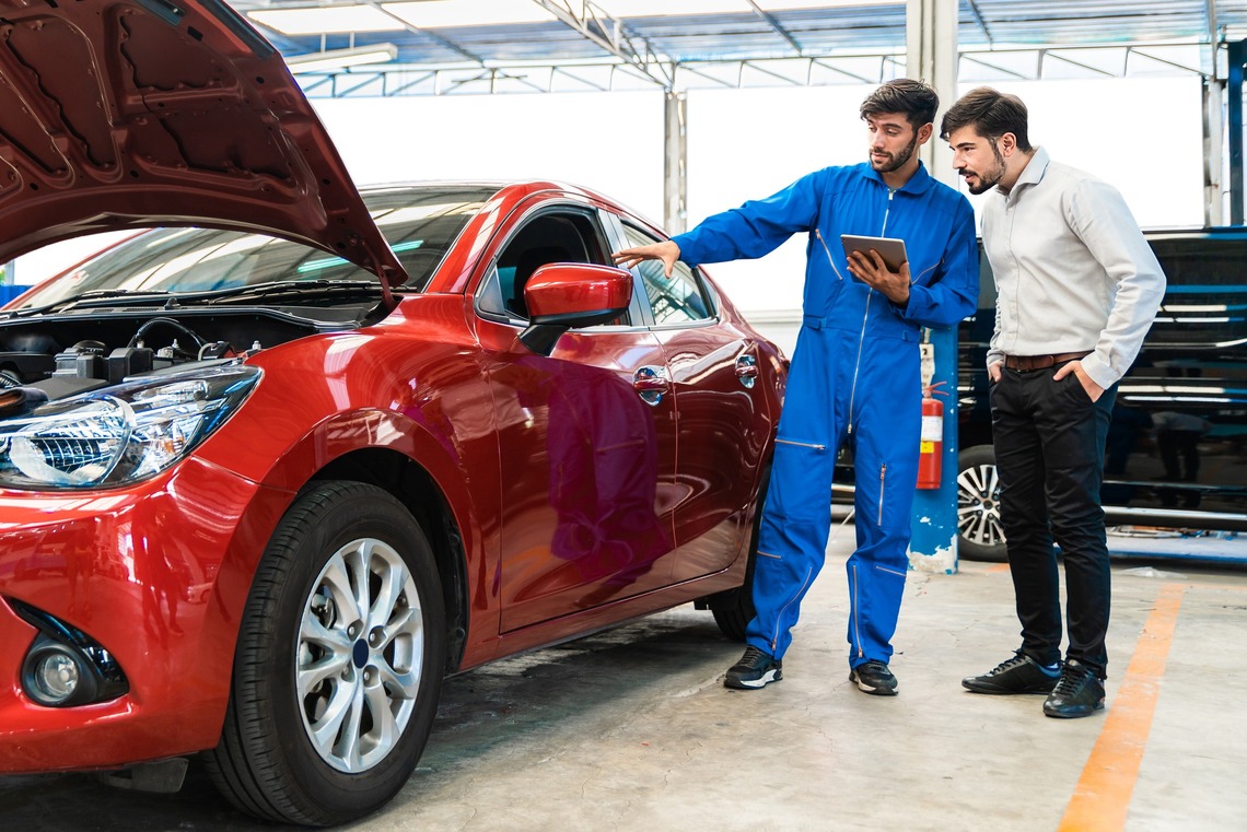 Ein Mann und ein Mechaniker unterhalten sich über ein rotes Auto | KFZ-Versicherug