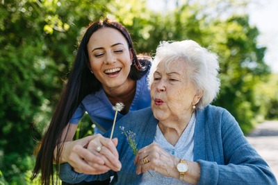 Oma und Enkelin pusten eine Pusteblume und sind glücklich