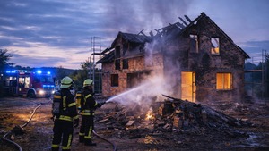 Feuerwehrkräfte löschen einen Brand an einem beschädigten Rohbau in der Bauphase bei einsetzender Dämmerung.
