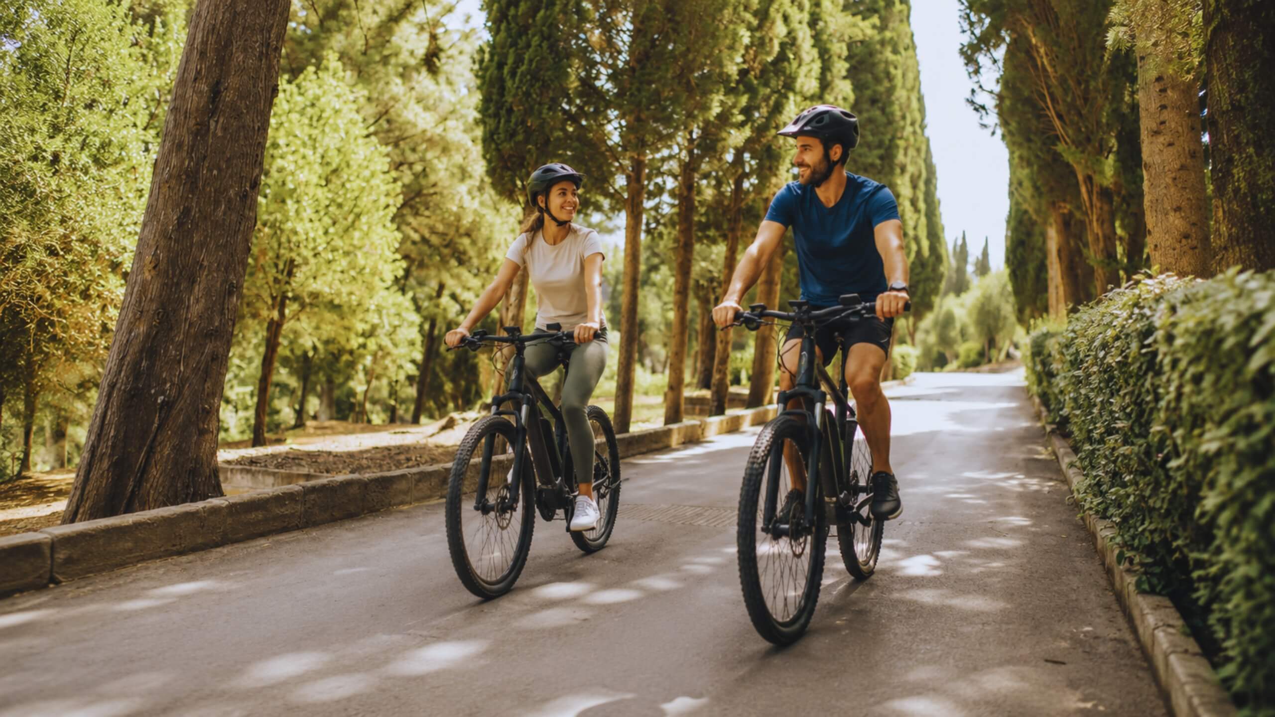 Zwei Radfahrer mit modernen E Bikes auf einem sonnigen Waldweg. Symbolbild für die Fahrrad und E Bike Versicherung mit Schutz bei Diebstahl, Unfällen und Schäden.